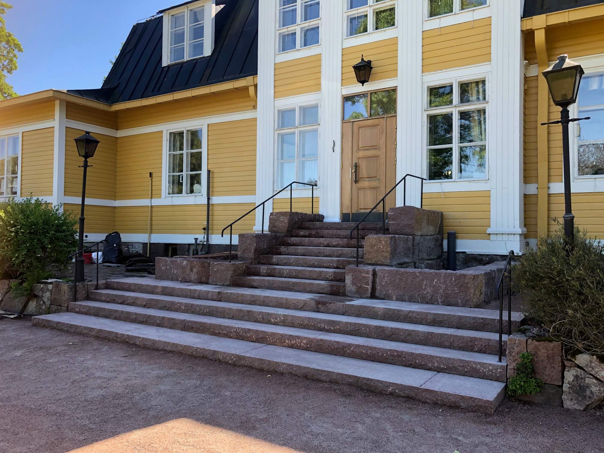 Keltaisen rakennuksen kiviset portaat johtavat puuovelle, jossa on mustat kaiteet ja lyhdyt molemmin puolin.