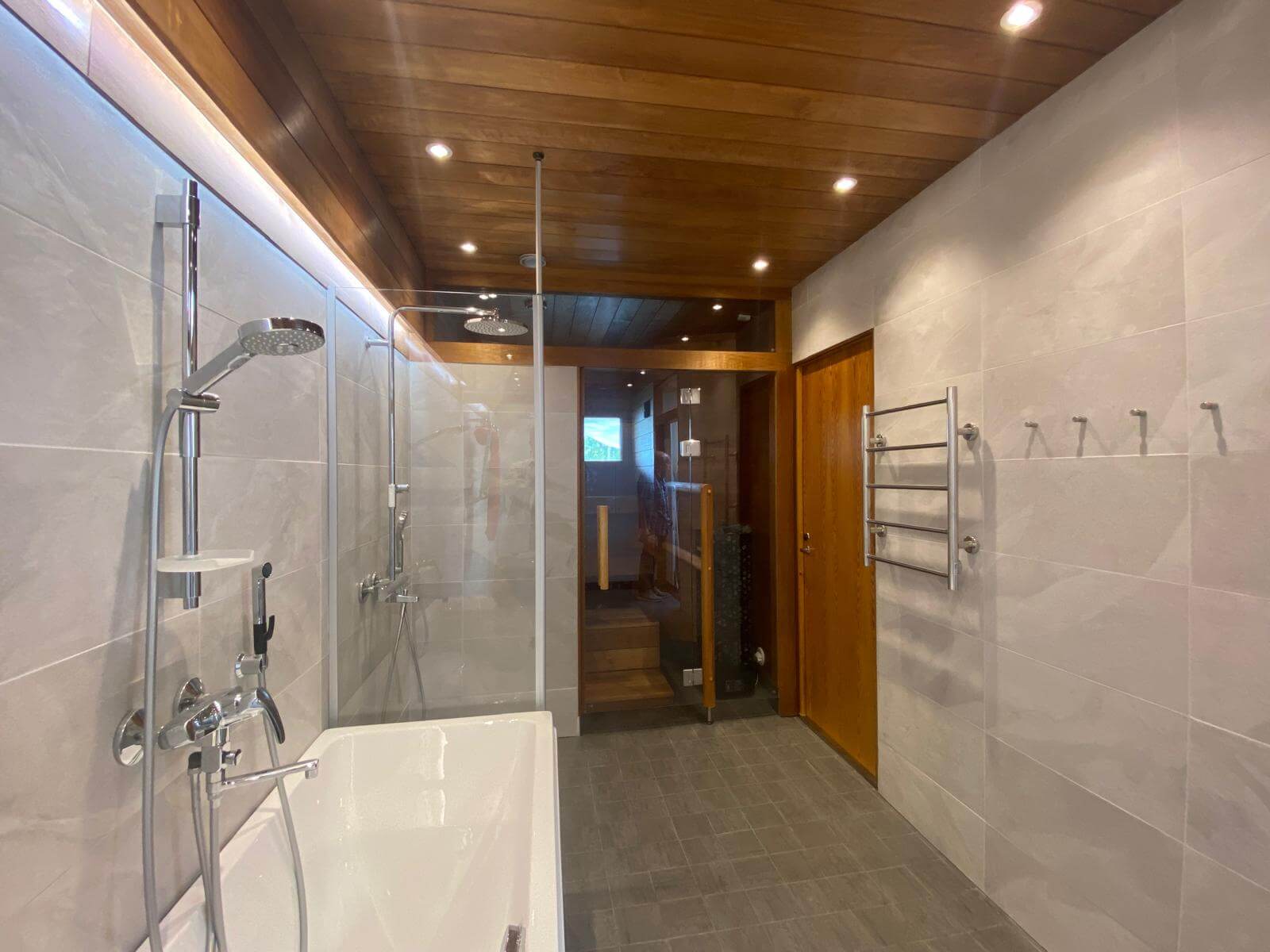 Kylpyhuoneen sisustus, jossa on suihku, kylpyamme, puinen katto ja pyyhekuivain. Valoisa ja moderni.