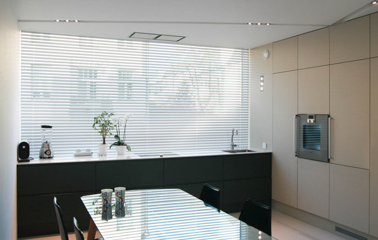 Moderni keittiö, jossa on suuri ikkuna, tummat kaapit, vaaleat seinät ja lasipöytä.