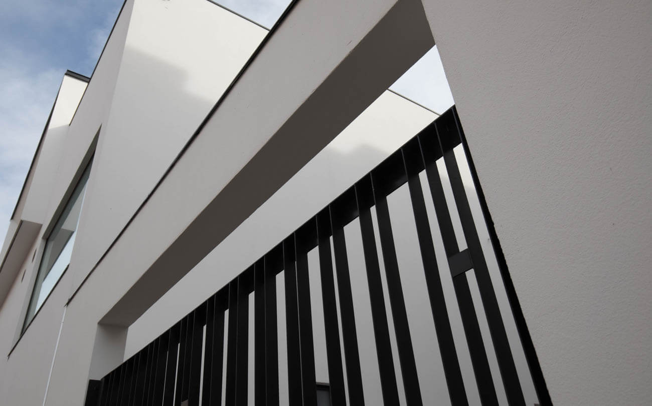 Modernin rakennuksen ulkokuva, jossa on valkoiset seinät ja musta metallinen säleikkö, valaistus on kirkas ja luonnollinen.