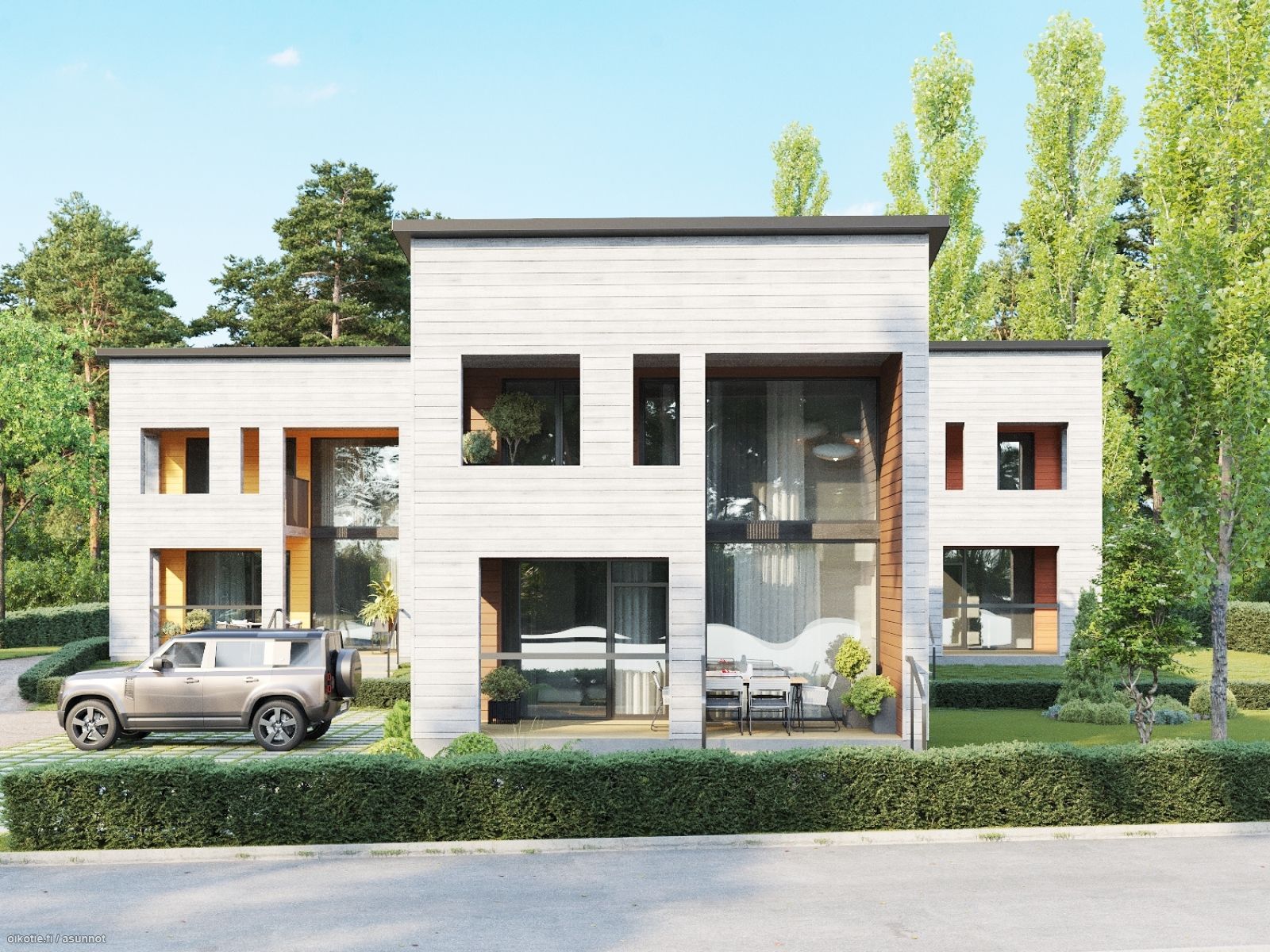 Moderni, valkoinen talo, jossa on suuret ikkunat, harmaa auto edessä ja vihreä pensasaita. Aurinkoinen sää.