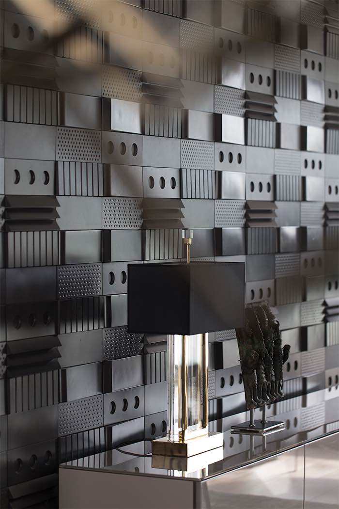 Musta seinäpaneeli, lamppu ja veistos kiiltävällä pöydällä.