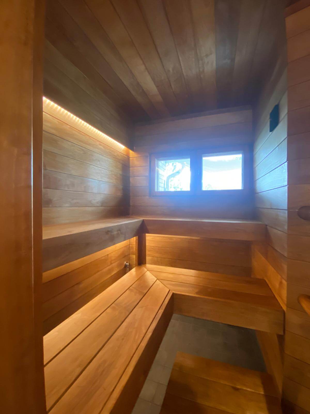 Puinen sauna, jossa on penkit, ikkuna ja epäsuora valaistus.