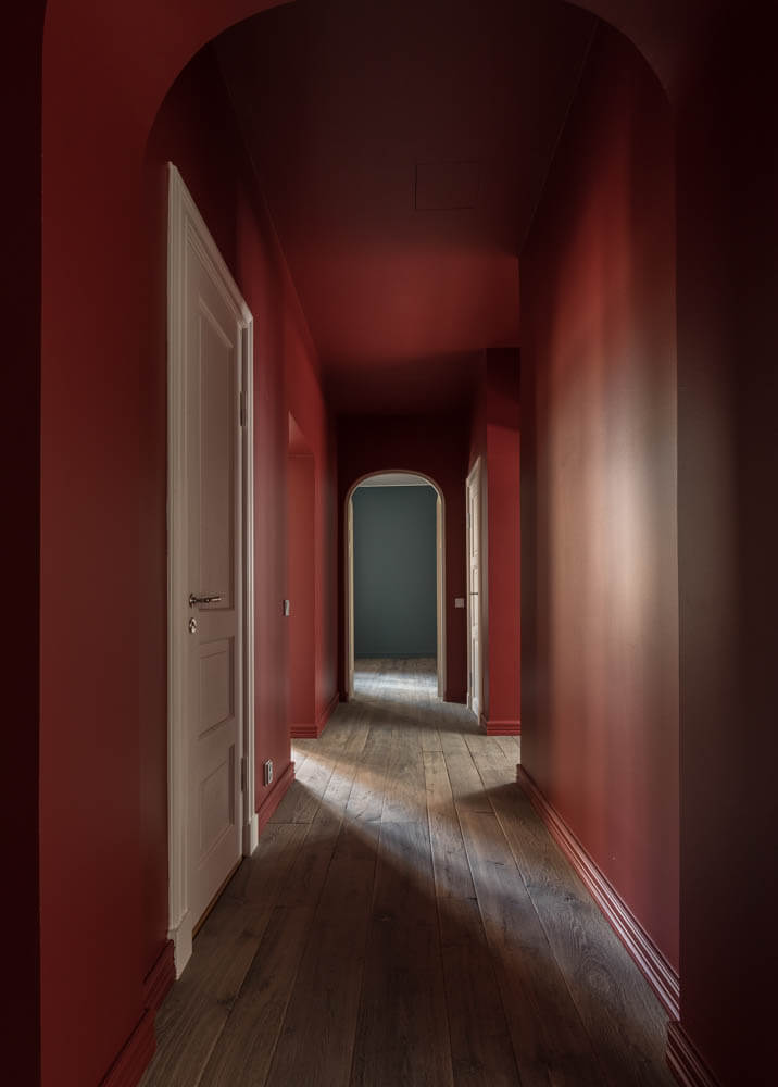 Punaisella maalattu käytävä, jossa on puulattia ja valkoiset ovet, valaistus luo tunnelmaa.