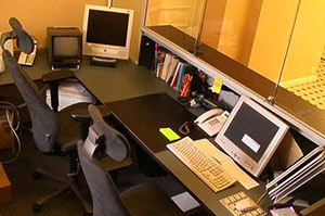Toimistohuoneessa on kaksi työpistettä, joissa on vanhanaikaiset tietokoneet, puhelin ja toimistotarvikkeita, valaistus on lämmin ja keinotekoinen.