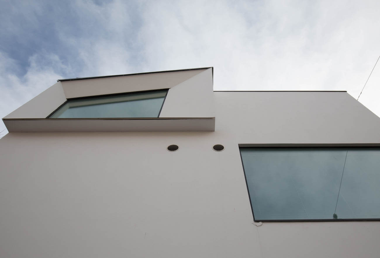 Moderni valkoinen rakennus, jossa on epäsymmetrisiä ikkunoita ja harmaa taivas taustalla.