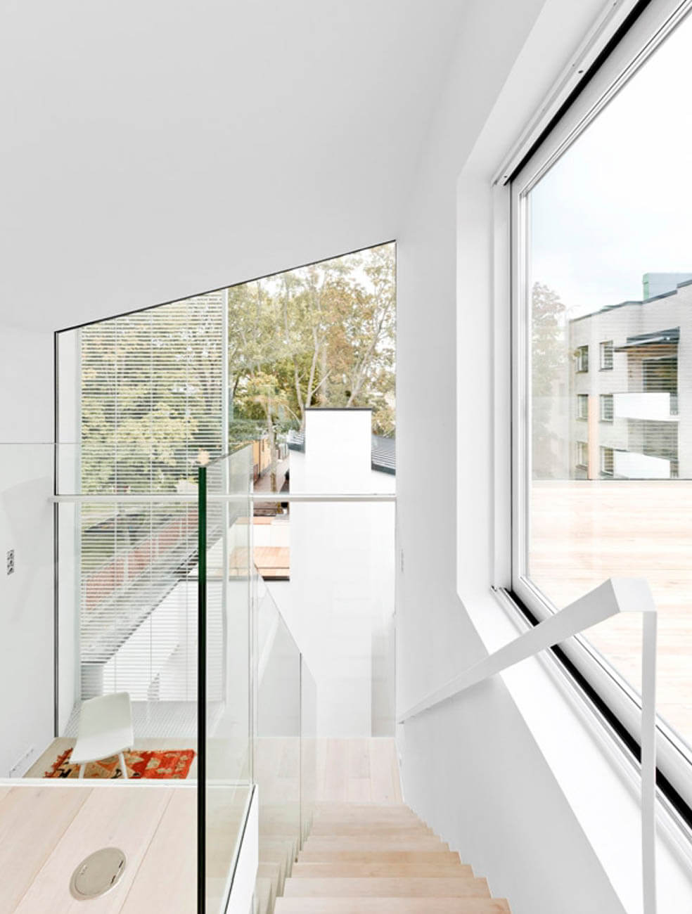 Valoisa sisätila, jossa on puuportaat, lasikaiteet ja suuret ikkunat, jotka tuovat luonnonvaloa ja näkymiä ulos.