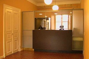 Sisäänkäynti ruskealla vastaanottotiskillä, valkoiset ovet ja lämmin valaistus.